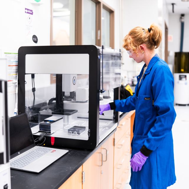BioPACIFIC MIP lab assistant Marissa Beyer loads an automated robotic liquid handler inside the laboratory.
