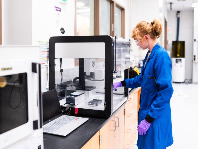 BioPACIFIC MIP lab assistant Marissa Beyer loads an automated robotic liquid handler inside the laboratory.